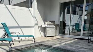 Ein Swimmingpool mit zwei Liegestühlen, einem Grill und einer Glastür, die zu einer Terrasse führt.