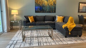 Ein modernes Wohnzimmer mit einem Ecksofa, einem Glastisch und einem großen Gemälde an der Wand.