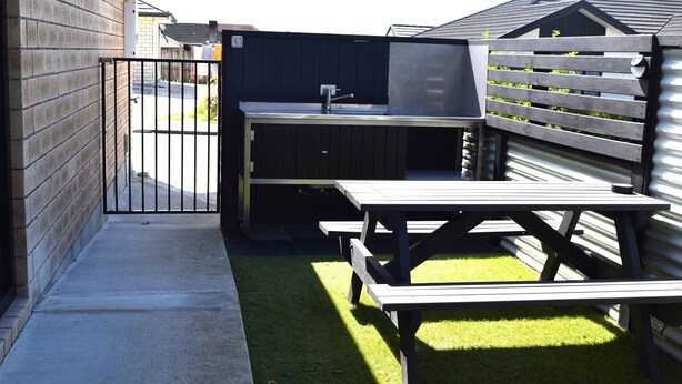 Ein Garten mit Grillplatz, Picknicktischen und einem umzäunten Spielbereich.