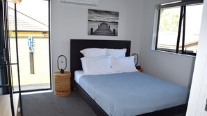 Ein Schlafzimmer mit Bett, Nachttisch, Lampe, einem Wandbild und einem Fenster.