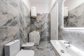 Une salle de bain avec des murs en marbre, des toilettes, un bidet, un lavabo et une baignoire.