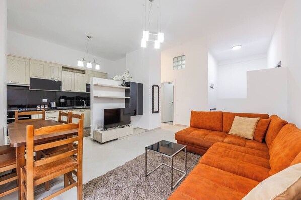Un salon moderne comprenant un canapé, un téléviseur et un coin repas avec des chaises et une table.