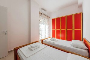 Une chambre d’hôtel avec deux lits simples, une armoire aux panneaux rouges et une fenêtre avec un rideau.