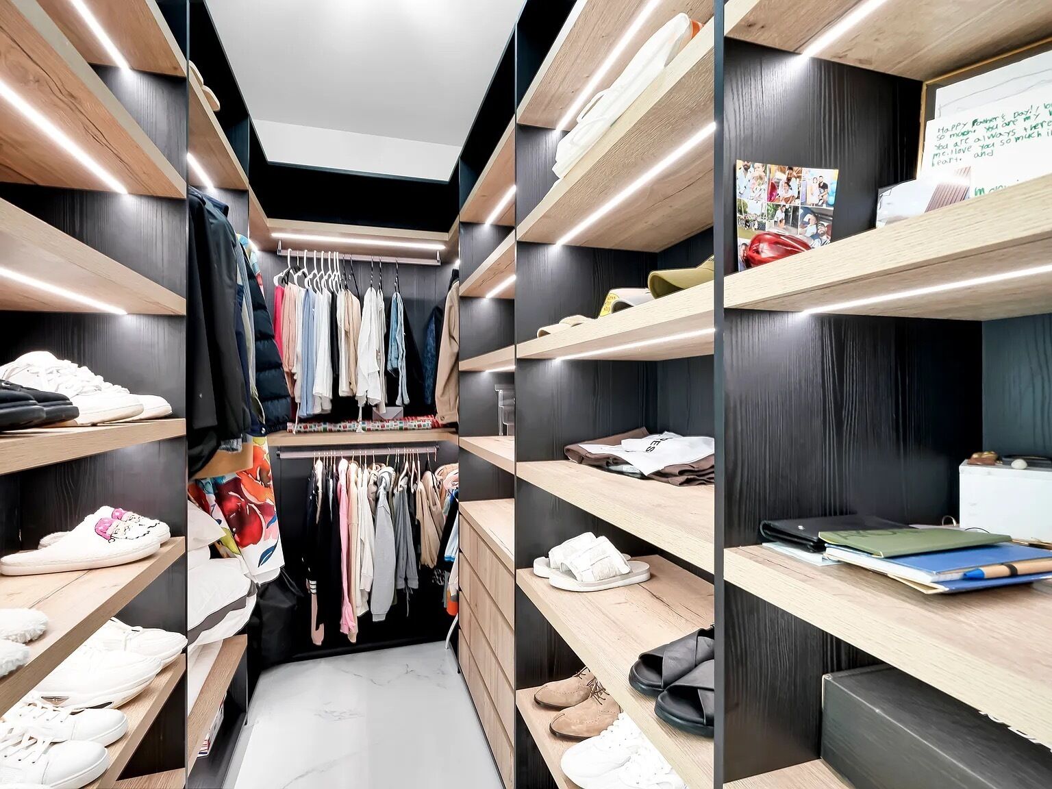 Un armario moderno con múltiples estantes para zapatos y ropa, una barra para colgar chaquetas y una pequeña zona de escritorio con un cuaderno y un bolígrafo.