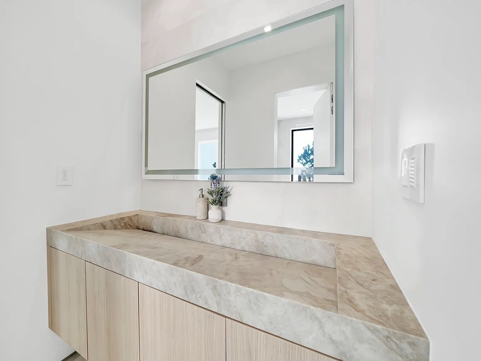 A bathroom with a large mirror, a marble countertop, and a wooden cabinet.