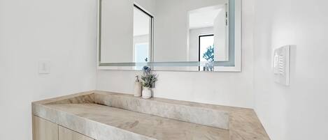 A bathroom with a large mirror, a marble countertop, and a wooden cabinet.