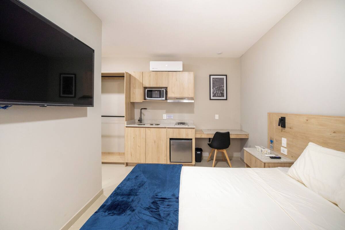 Een hotelkamer met een bed, een bureau met stoel, een magnetron, een kleine koelkast en een aan de muur bevestigde televisie.