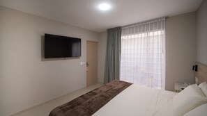 A hotel room with a bed, a television mounted on the wall, a door, and a window with curtains. - Hotel Puerta Gala 2903 (Guadalajara)