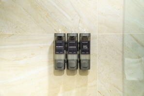 Three hand-poured bottles of shampoo, conditioner, and body wash on a marble wall. - Hotel Puerta Gala 2903 (Guadalajara)