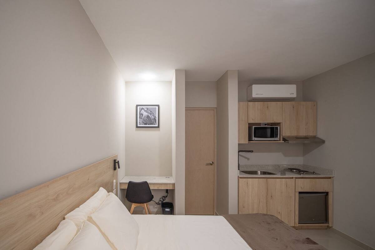 Een slaapkamer met een bed, een bureau, een stoel, een magnetron, een wastafel en een deur naar een badkamer.