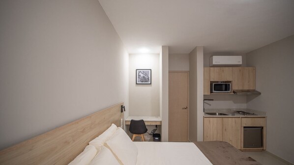 A bedroom with a bed, a desk, a chair, a microwave, a sink, and a door leading to a bathroom. - Hotel Puerta Gala 2903 (Guadalajara)