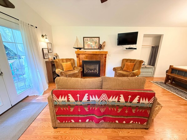 A living room with a fireplace, two armchairs, a sofa, a television, and a door leading to an outdoor area. - ‘Spruce’ Riverfront Cabin near Olympic National Park (Beaver)