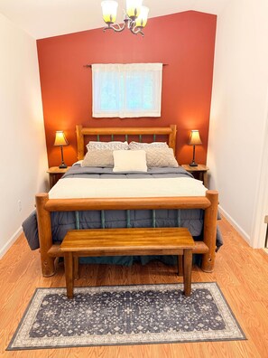 Ein Schlafzimmer mit einem hölzernen Bett, zwei Nachttischlampen, einem Fenster mit durchsichtigen Vorhängen und einem gemusterten Teppich.
