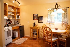 A compact kitchen with wooden cabinets, a stove, a microwave, and a dining area with a table and chairs.