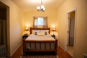 A bedroom with a wooden bed, two bedside lamps, a chandelier, and a window with curtains.