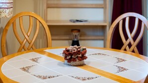Uma mesa de jantar com toalha de mesa florida, duas cadeiras, um candelabro com chifres de veado e uma estante de livros ao fundo.
