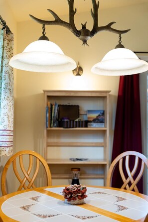 A dining table with a floral tablecloth, two chairs, a chandelier with antlers, and a bookshelf in the background. - ‘Spruce’ Riverfront Cabin near Olympic National Park (Beaver)