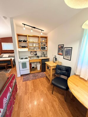 A compact kitchen with a stove, microwave, and wooden shelves. There's a dining area with a table and chairs. - ‘Spruce’ Riverfront Cabin near Olympic National Park (Beaver)
