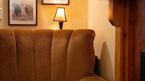 Um sofá marrom num quarto com uma luminária e quadros nas paredes.