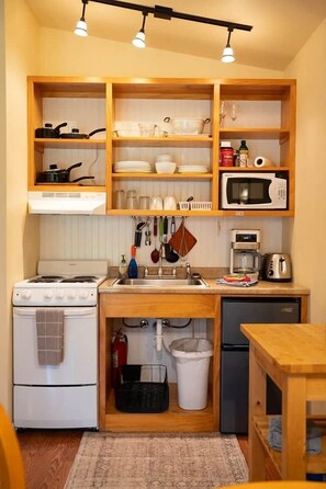 Une cuisine compacte équipée d’une cuisinière, d’un four à micro-ondes, d’un évier et d’étagères en bois.