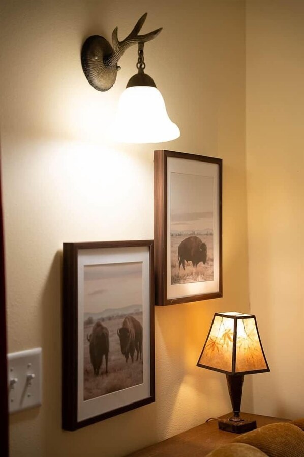 A wall-mounted light fixture with a deer head, two framed photographs of bison, and a table lamp. - ‘Spruce’ Riverfront Cabin near Olympic National Park (Beaver)