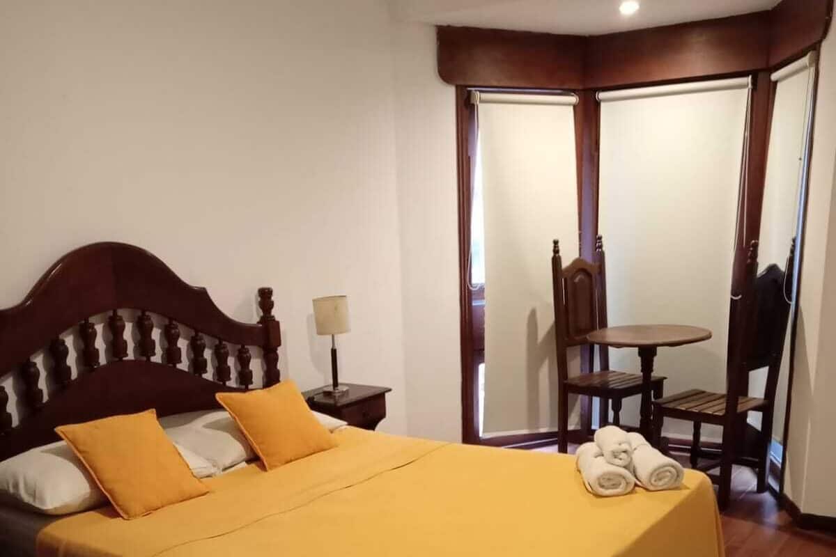 A neatly made bed with a yellow bedspread, a wooden headboard, and a nightstand with a lamp.