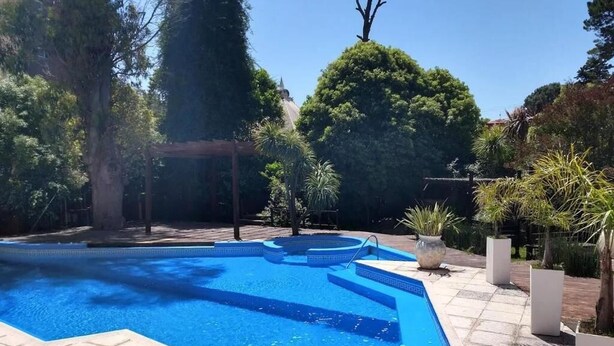 Una piscina con bordeado de baldosas, rodeada de árboles y plantas en macetas.