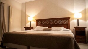 Una cama bien hecha con cabecera de madera, dos mesitas de noche con lámparas y una cómoda pequeña.