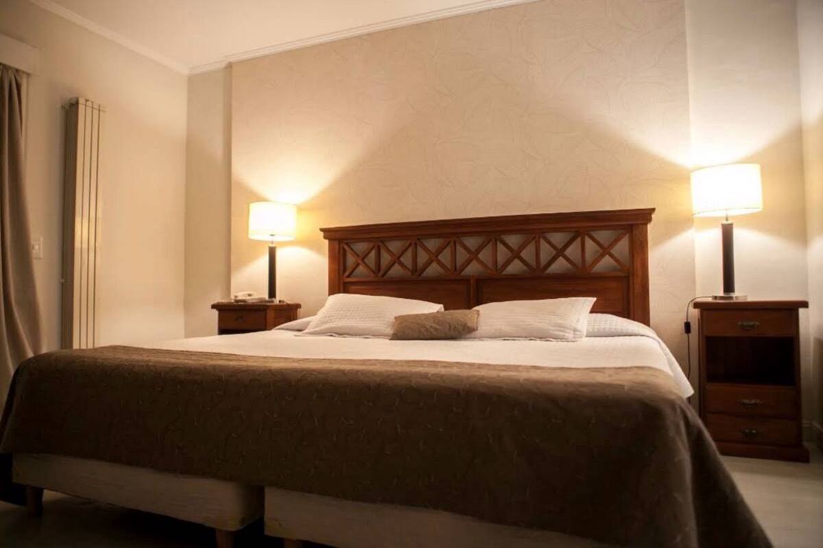 A neatly made bed with a wooden headboard, two bedside tables with lamps, and a small drawer unit.