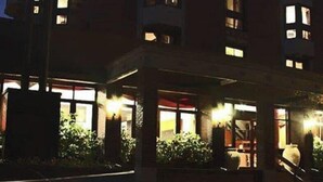Un edificio de varios pisos con ventanas iluminadas, una entrada a nivel de calle y una escalera visible que conduce a la entrada.