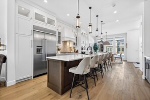 A modern kitchen with white cabinetry, stainless steel appliances, and a central island with bar stools. - Modern Pet‑Friendly Altadore Gourmet Kitchen (Calgary)
