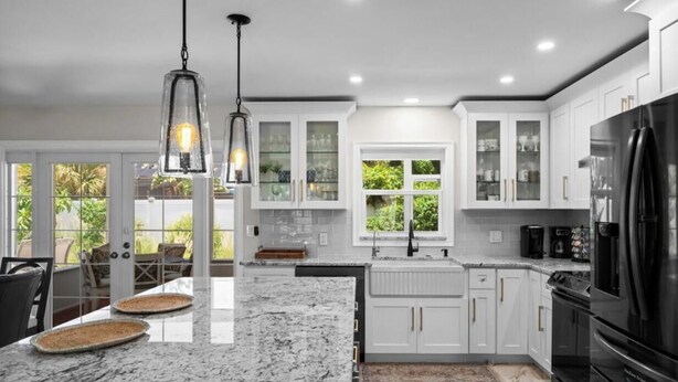 A modern kitchen with white cabinets, granite countertops, a black refrigerator, and pendant lighting. - Serene 3-bedroom house with AC in charming Venice (Venice)