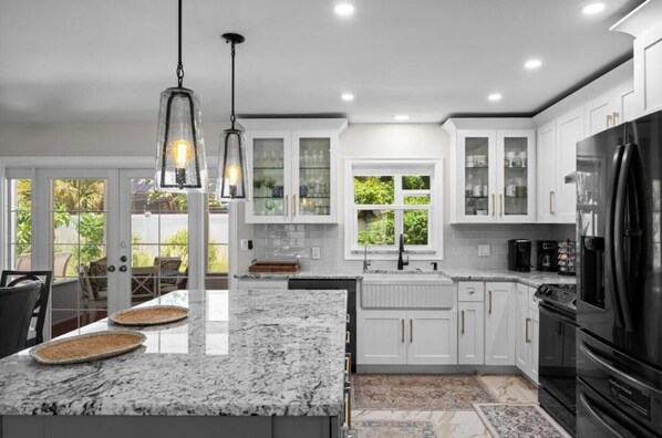 A modern kitchen with white cabinets, granite countertops, a black refrigerator, and pendant lighting. - Serene 3-bedroom house with AC in charming Venice (Venice)