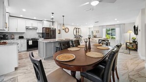 A modern kitchen with white cabinetry, a central island, and a dining area with a wooden table and chairs. - Serene 3-bedroom house with AC in charming Venice (Venice)
