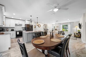 A modern kitchen with white cabinetry, a central island, and a dining area with a wooden table and chairs. - Serene 3-bedroom house with AC in charming Venice (Venice)