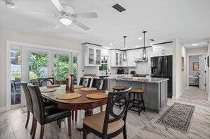 A modern kitchen with white cabinets, a black refrigerator, and a dining area with a round table and chairs. - Serene 3-bedroom house with AC in charming Venice (Venice)