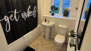 Een badkamer met een zwart douchegordijn, een witte wastafel, toilet en een raam met uitzicht.