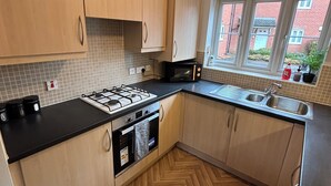 Een moderne keuken met houten kastjes, een gasfornuis, een oven, een spoelbak en een raam met uitzicht op een bakstenen gebouw.