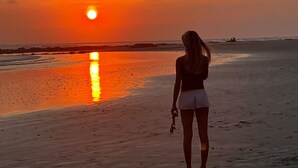 En person står på en strand och tittar mot solnedgången.