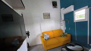 Een kamer met een gele bank, een klein rond tafeltje en een witte deur.