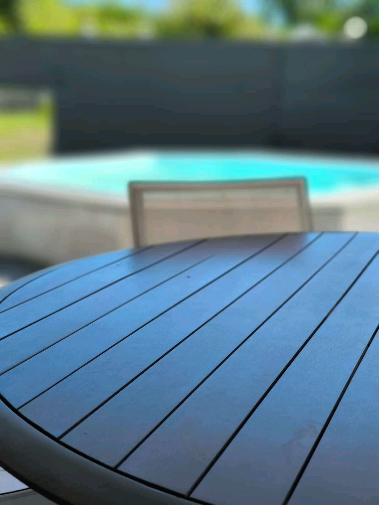 A round wooden table with a metal frame, positioned in front of a swimming pool.