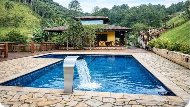 A pool with a waterfall feature, surrounded by a stone patio and a wooden fence.