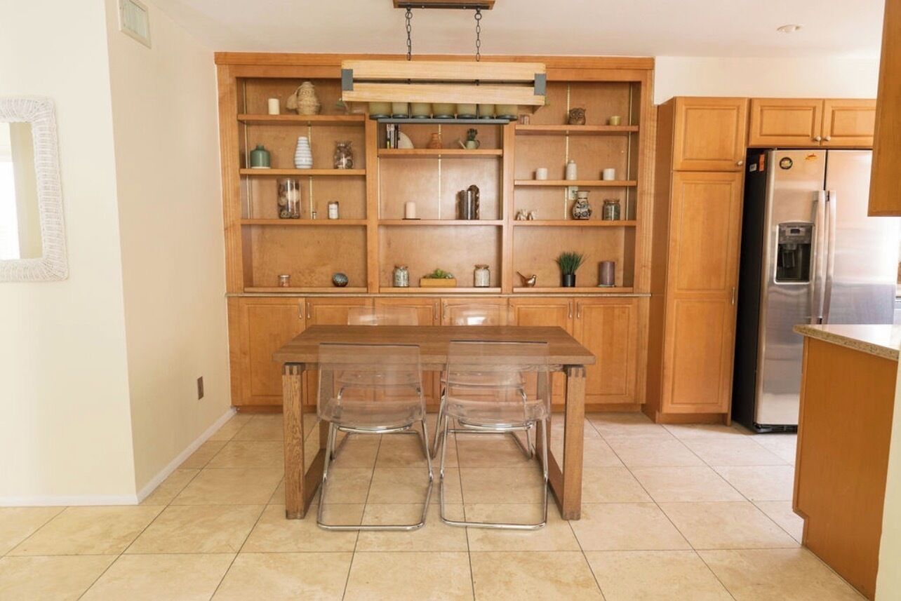 Une cuisine avec des meubles en bois, un réfrigérateur en acier inoxydable et une table à manger avec des chaises transparentes.