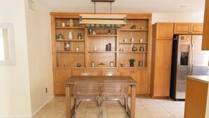 Una cocina con armarios de madera, un refrigerador de acero inoxidable y una mesa de comedor con sillas transparentes.