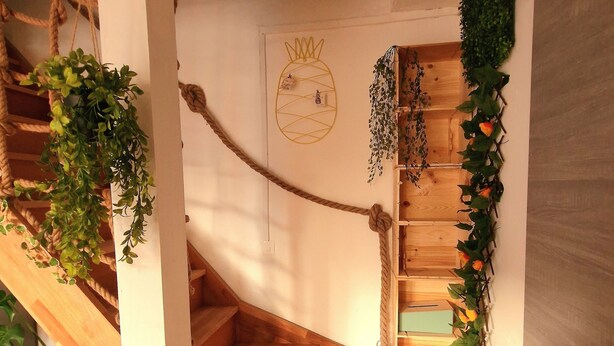 A wooden staircase with a rope handrail, surrounded by greenery and a pineapple wall art piece. - Cozy House Near the Castle & Lakeside Leisure Area (Cepoy)