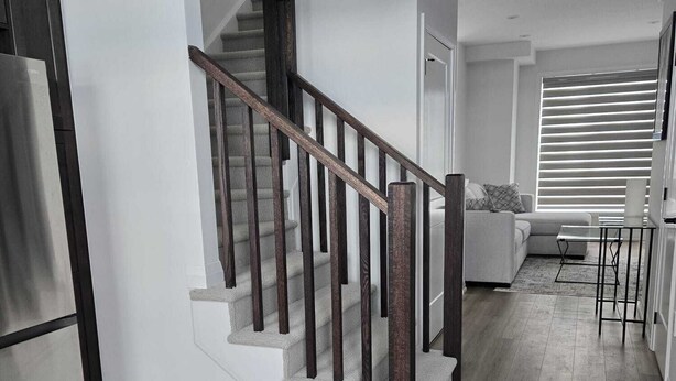 Una cocina moderna con refrigerador empotrado, piso de madera y una escalera con barandillas de madera oscura.