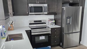 Una cocina moderna con armarios oscuros, electrodomésticos de acero inoxidable y encimera blanca.