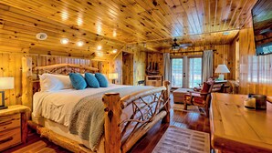 A wooden cabin interior with a large bed, a wooden desk, and a dining table. - Lakefront Luxury w/ Dock + Fenced Yard (Blairsville)
