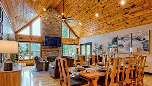 A spacious dining area with wooden furniture, large windows, and a stone wall. - Lakefront Luxury w/ Dock + Fenced Yard (Blairsville)