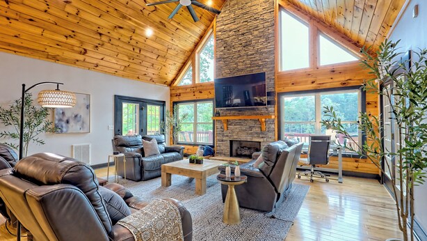 A spacious living room with leather sofas, a stone fireplace, and large windows. - Lakefront Luxury w/ Dock + Fenced Yard (Blairsville)